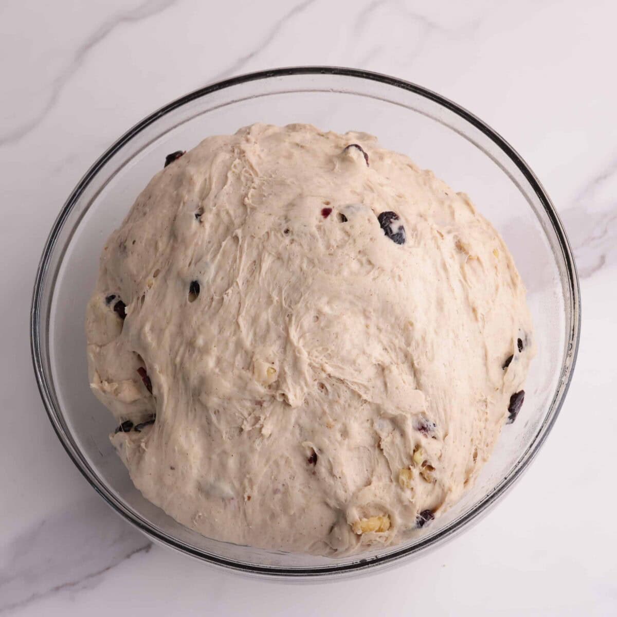 A greased, glass bowl with the mixed dough shaped into a bowl inside, ready to be covered by plastic wrap to rise.