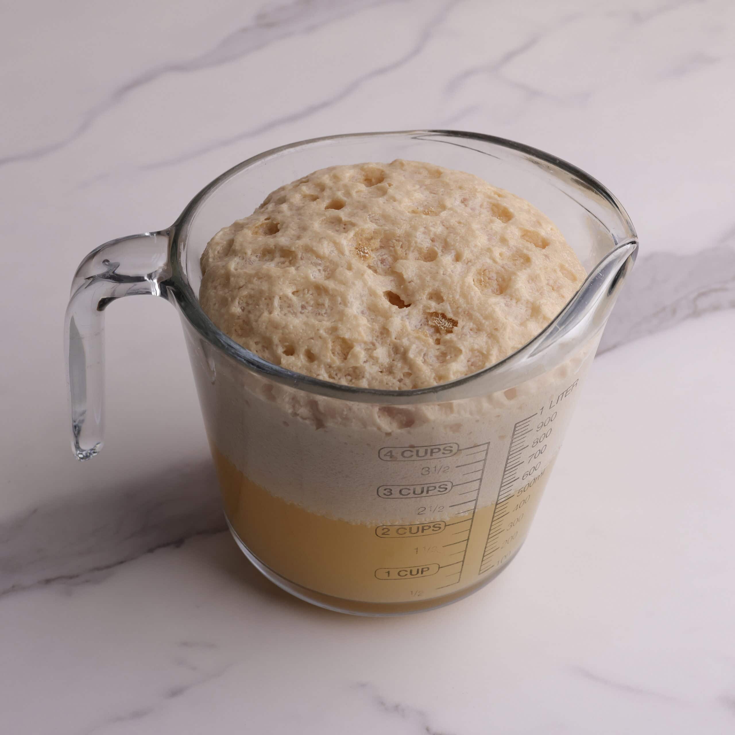A measuring cup of activated yeast, showing that when it is ready you will have about half water and half bubbled yeast on top.