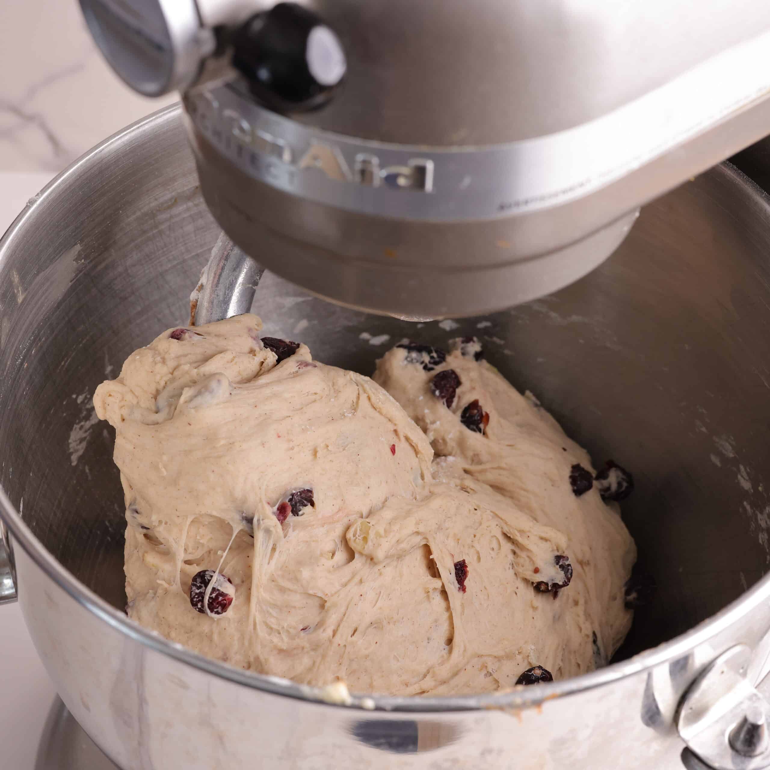 A mixer with the dough wrapped around the dough hook showing how it will come together as a ball when it is ready.