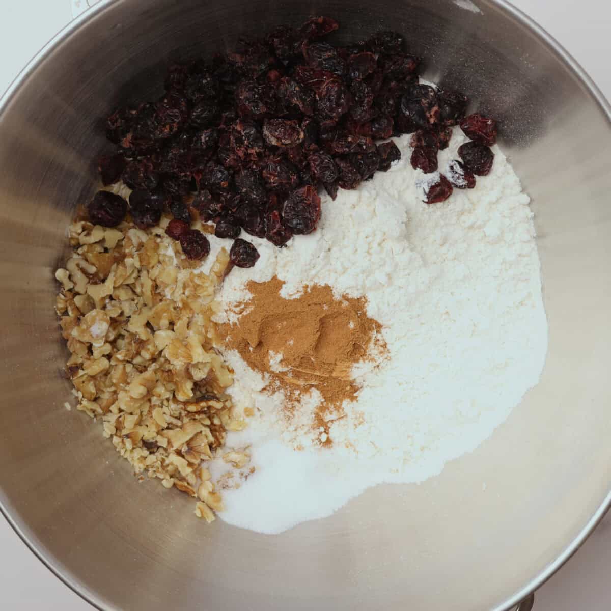 A mixing bowl with all dry ingredients - flour, salt, cinnamon, craisins and walnuts - in it.