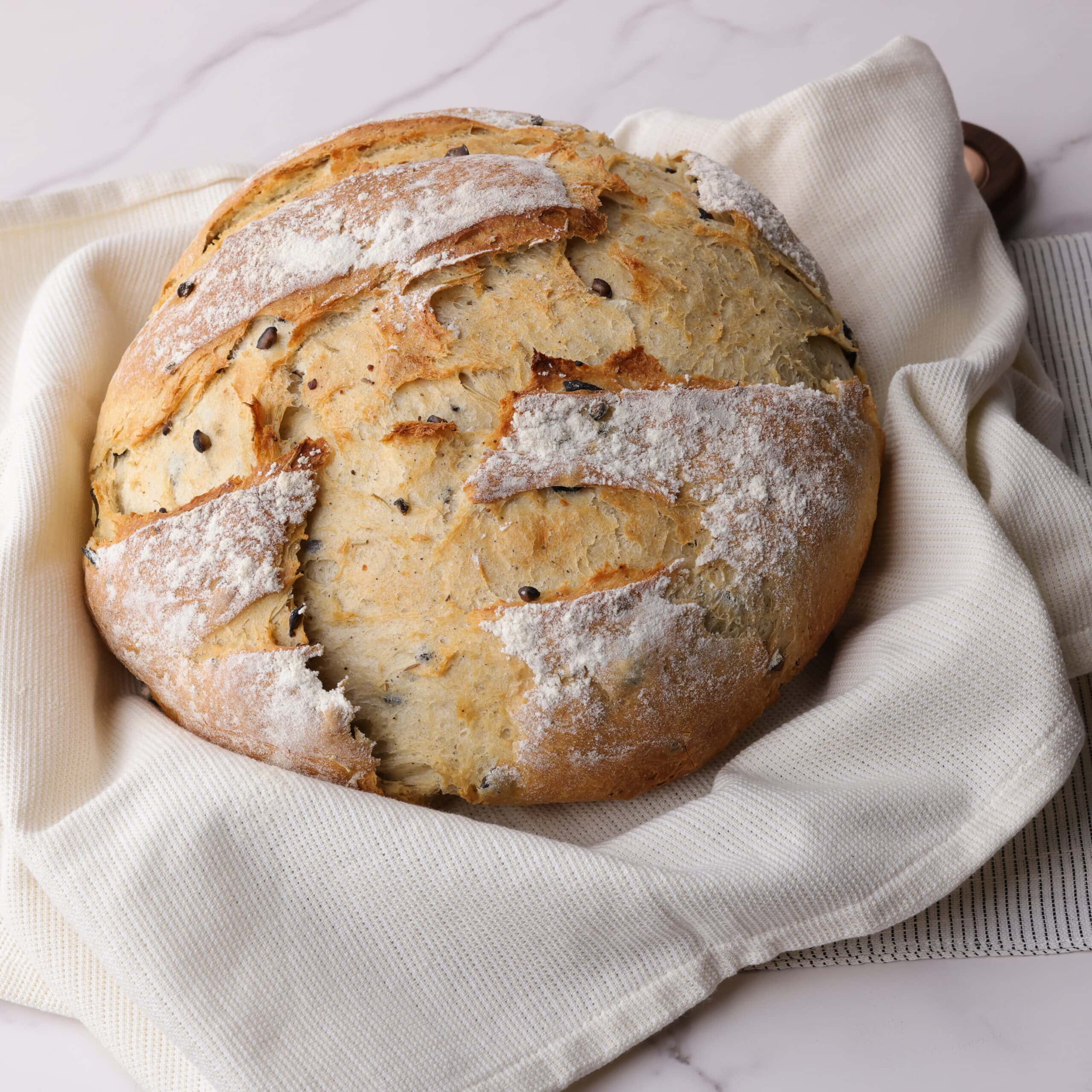 A whole cooked loaf of baked Rosemary Garlic Bread decoratively displayed on a tea towel.