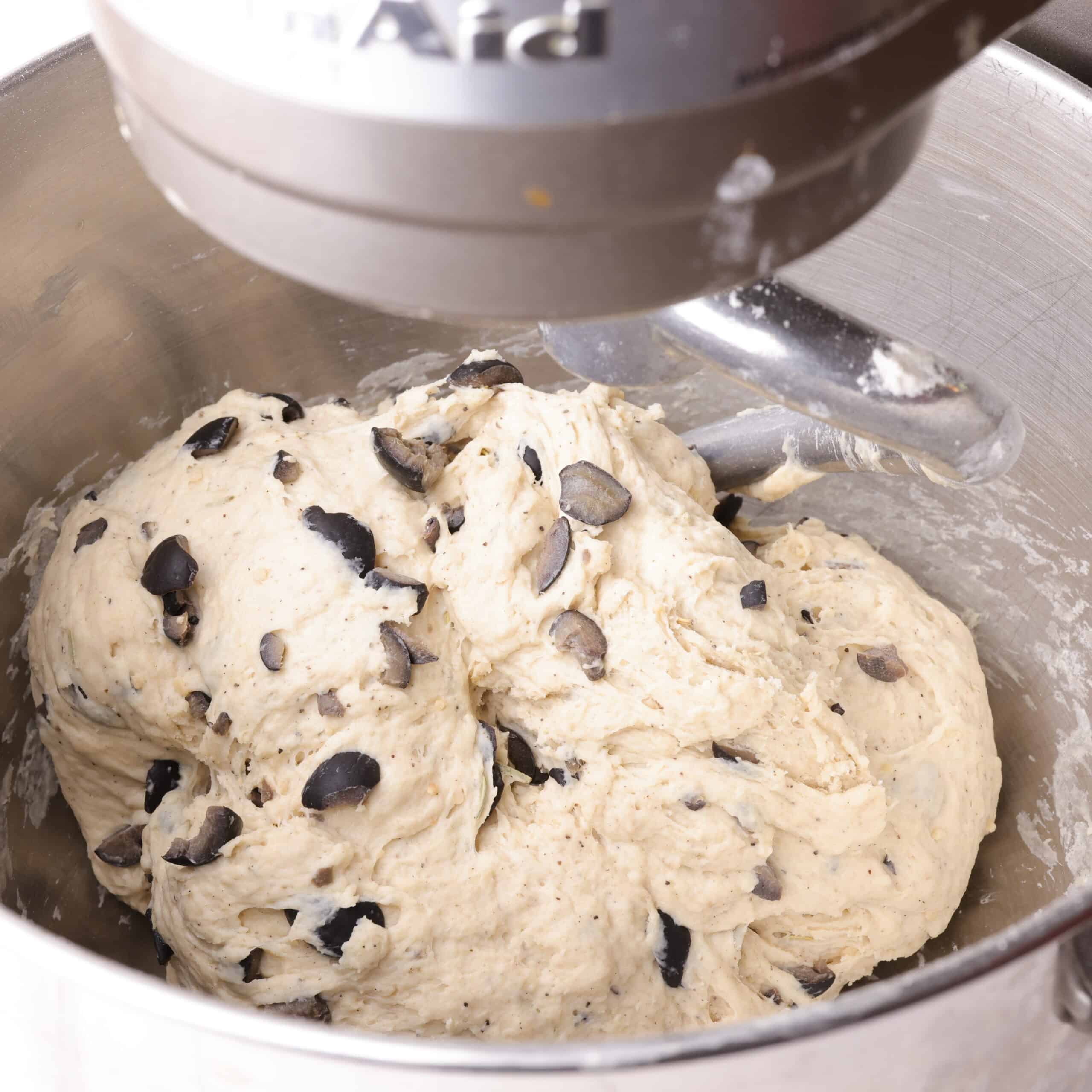 A mixer with the dough wrapped around the dough hook showing how it will come together as a ball when it is ready.