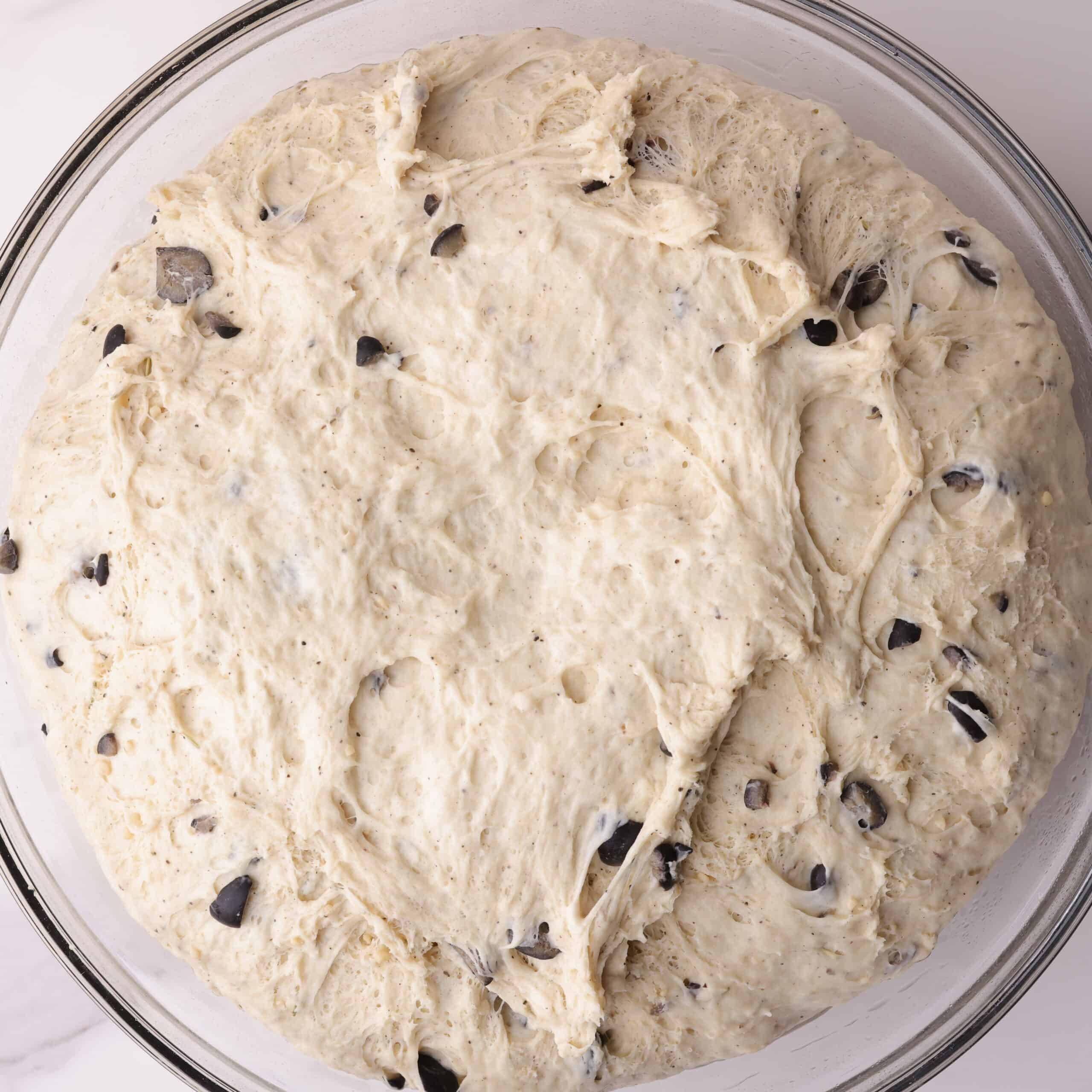 A greased, glass bowl with the mixed dough shaped into a bowl inside, ready to be covered by plastic wrap to rise.
