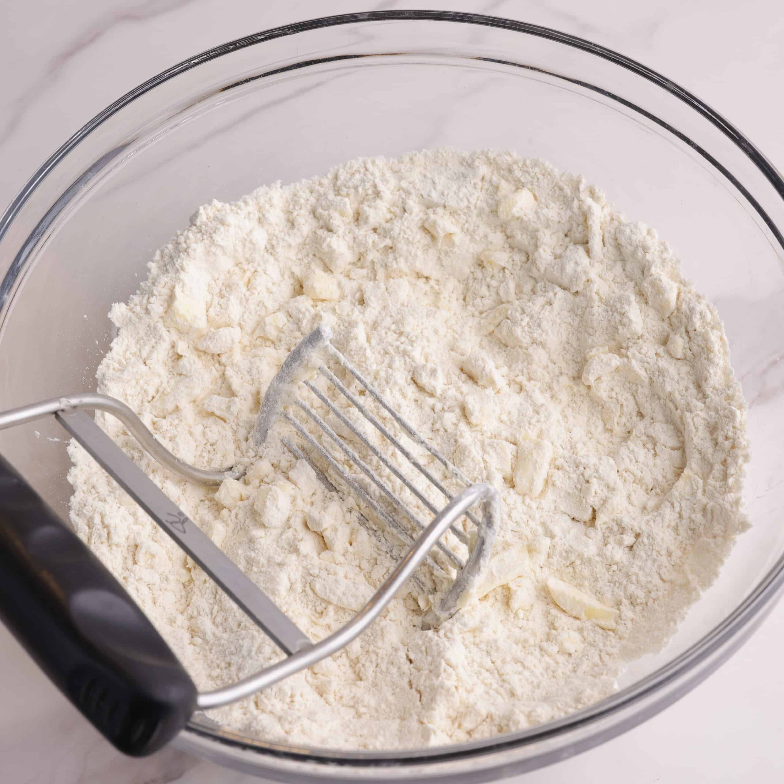 A bowl with flour and the cold butter cut in using a pastry cutter.