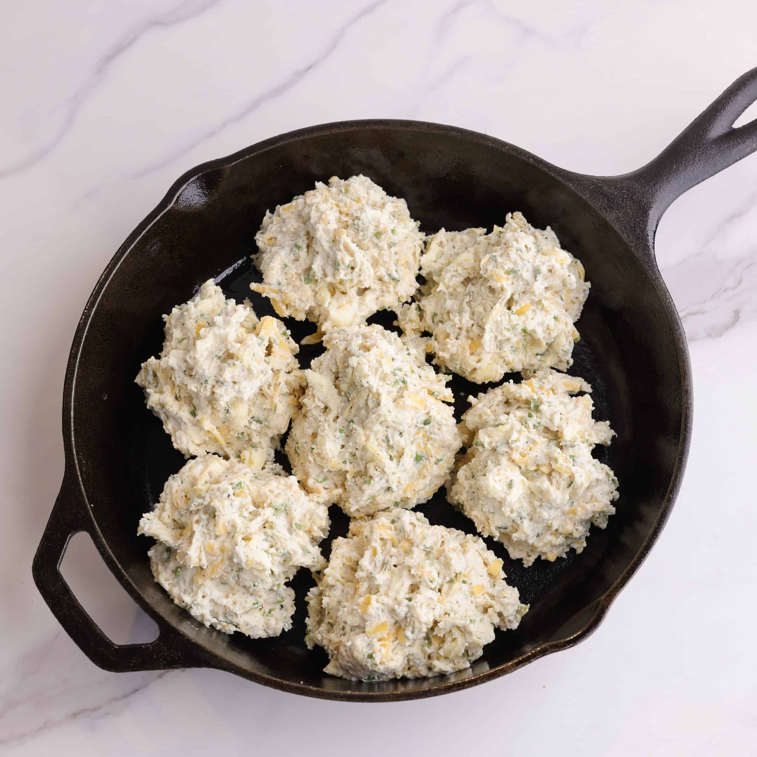 An ungreased skillet with the biscuit dough dropped as biscuits in it - 6 around the outside and one in the middle.