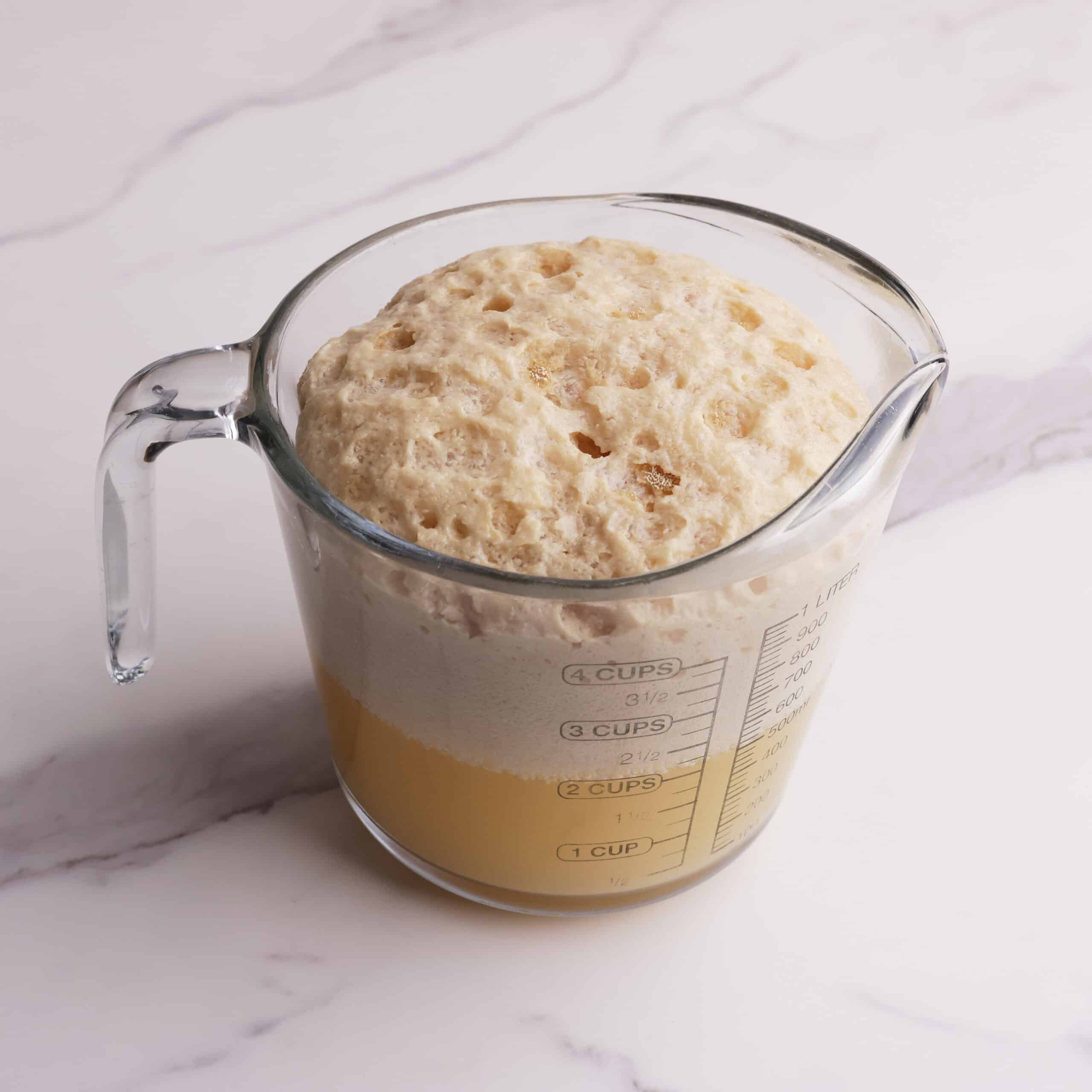 A measuring cup of activated yeast, showing that when it is ready you will have about half water and half bubbled yeast on top.