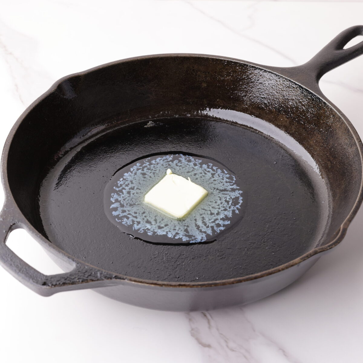 A cube of butter melting in a cast iron skillet.