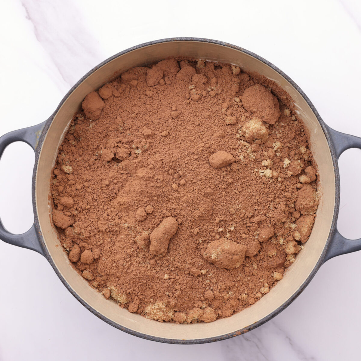 The batter in the enameled cast iron pot with the cocoa powder and brown sugar topping on it.