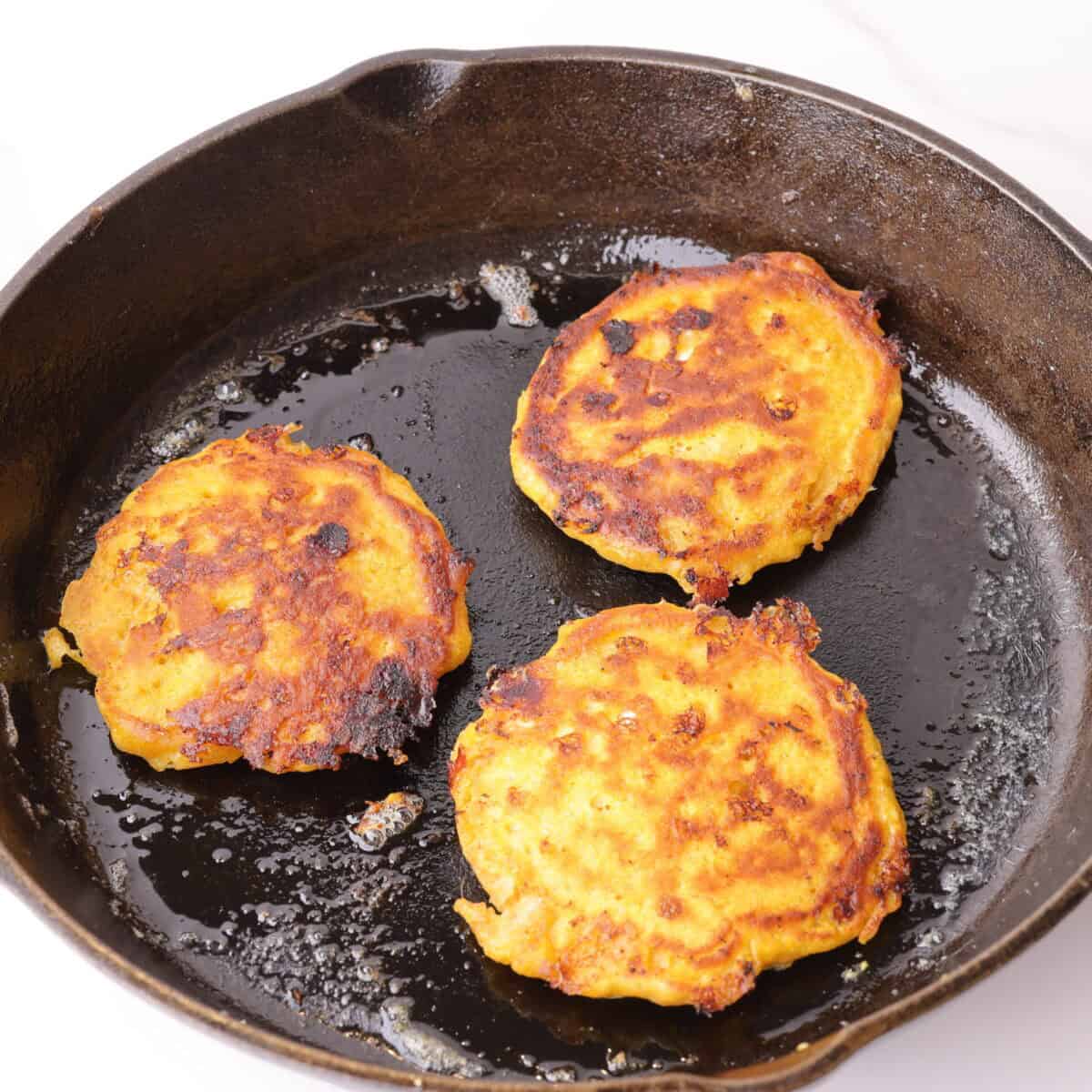 Three flipped pancakes, cooked to golden perfection in a hot cast iron skillet.