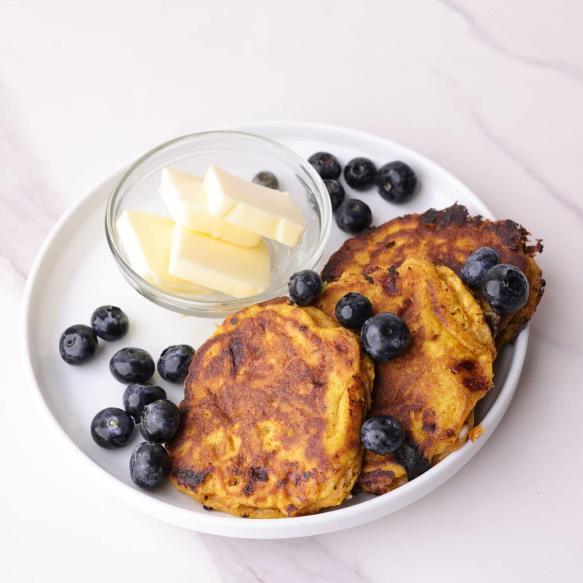 Pumpkin cottage cheese pancakes decoratively plated with blueberries and butter on a white plate.