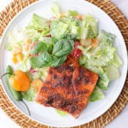 A plate of crisp romaine lettuce, mixed with sweet bell peppers, cherry tomatoes and seasoned croutons, all tossed in Caesar dressing and topped with a perfectly baked blackened salmon fillet. Garnished with basil and spicy peppers.