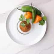 A bowl of blackened seasoning garnished with parsley and displayed with a variety of spicy peppers, jalapeño, habanero and serrano to demonstrate it's spicy flavor.