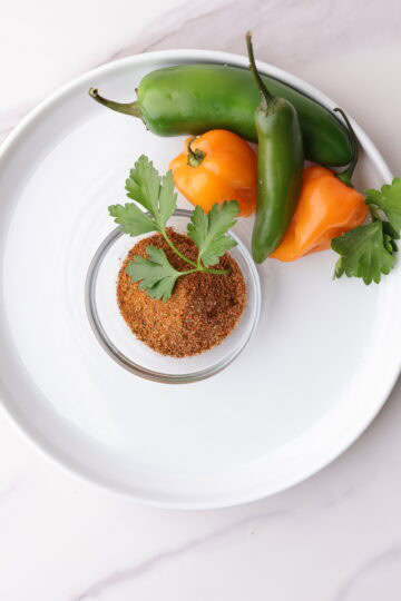 A bowl of blackened seasoning garnished with parsley and displayed with a variety of spicy peppers, jalapeño, habanero and serrano to demonstrate it's spicy flavor.