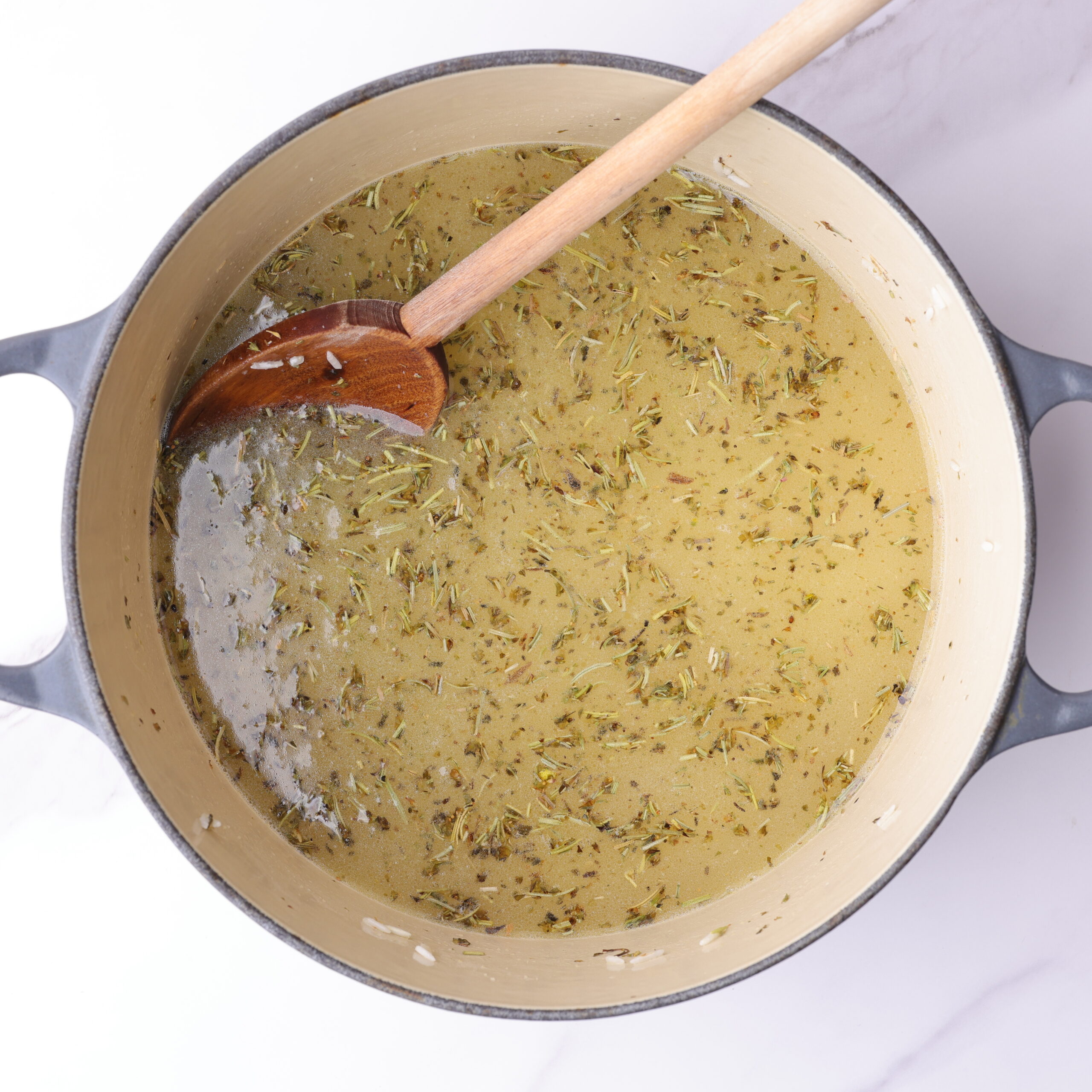 The chicken broth and water poured over the sautéd rice and spices. The liquids cover the rice while the herbs float to the top.