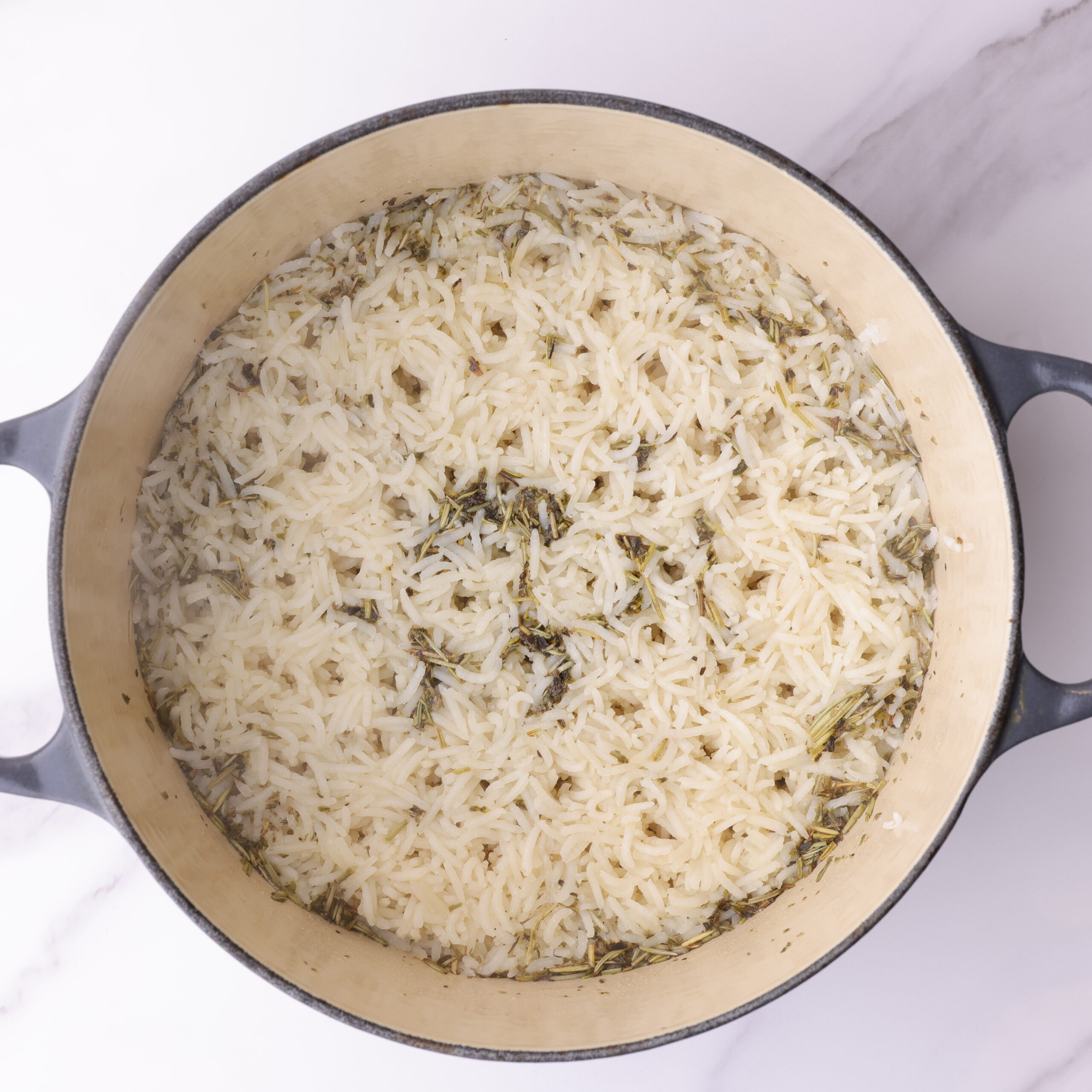 Steaming rosemary basmati rice cooked until tender in the medium sized pot. The rice and herbs slightly separate.