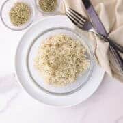 Tender basmati rice, cooked with the aromatic additions of rosemary and thyme., displayed in a bowl with a fork and knife, topped with rosemary and bowls of rosemary and thyme beside it for visual appeal.