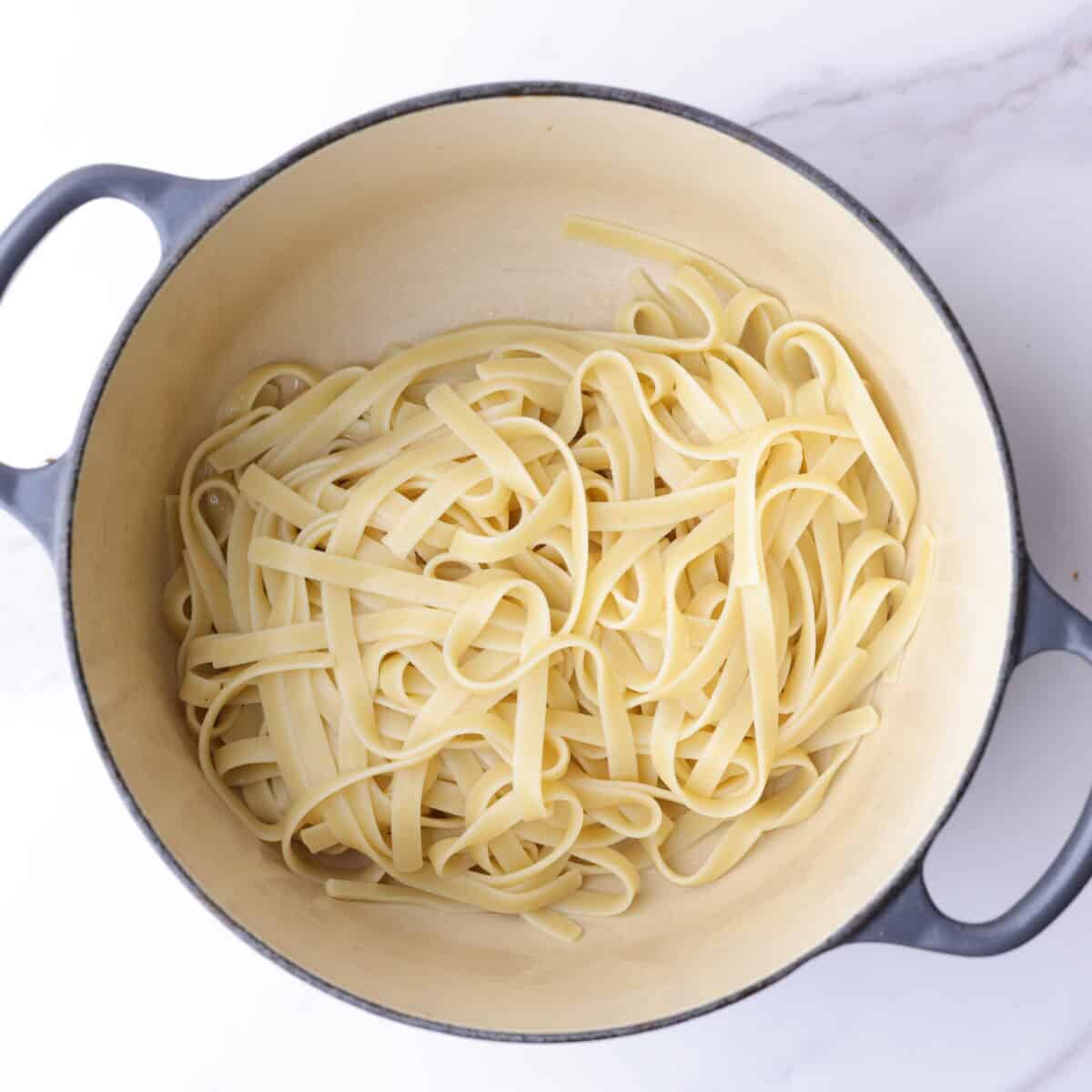 A small enameled pot with tenderly cooked fettuccine noodles.