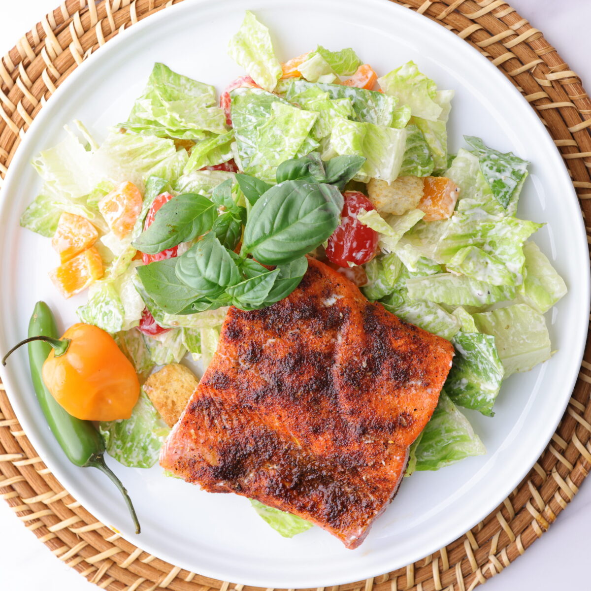 A plate of crisp romaine lettuce, mixed with sweet bell peppers, cherry tomatoes and seasoned croutons, all tossed in Caesar dressing and topped with a perfectly baked blackened salmon fillet. Garnished with basil and spicy peppers.