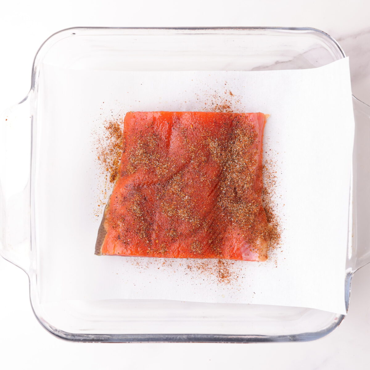 A 4 ounce red salmon fillet in a glass baking dish on parchment paper, lightly oiled and sprinkled with the blackened seasoning mix. 