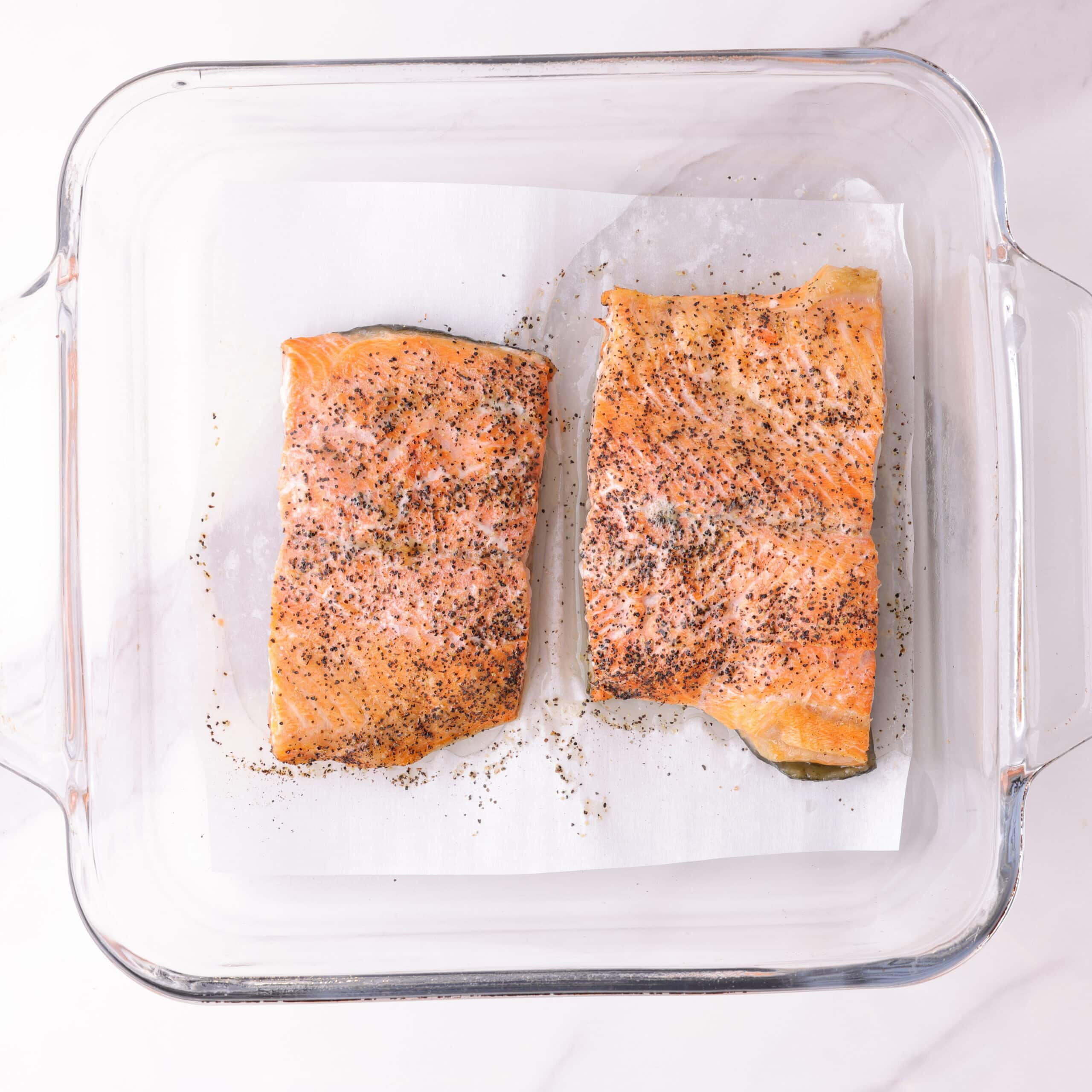 Two 3 ounce salmon fillets baked to tender flakiness in glass baking dish.