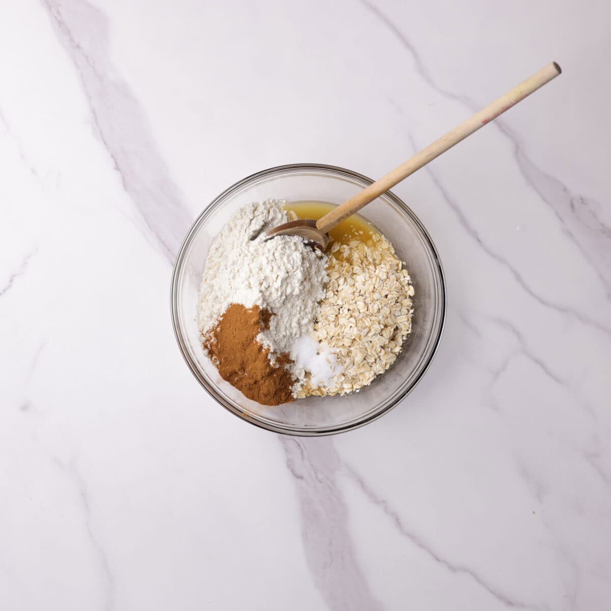A bowl with the butter and sugar mixture topped with the dry ingredients - flour, oats, cinnamon and salt. 