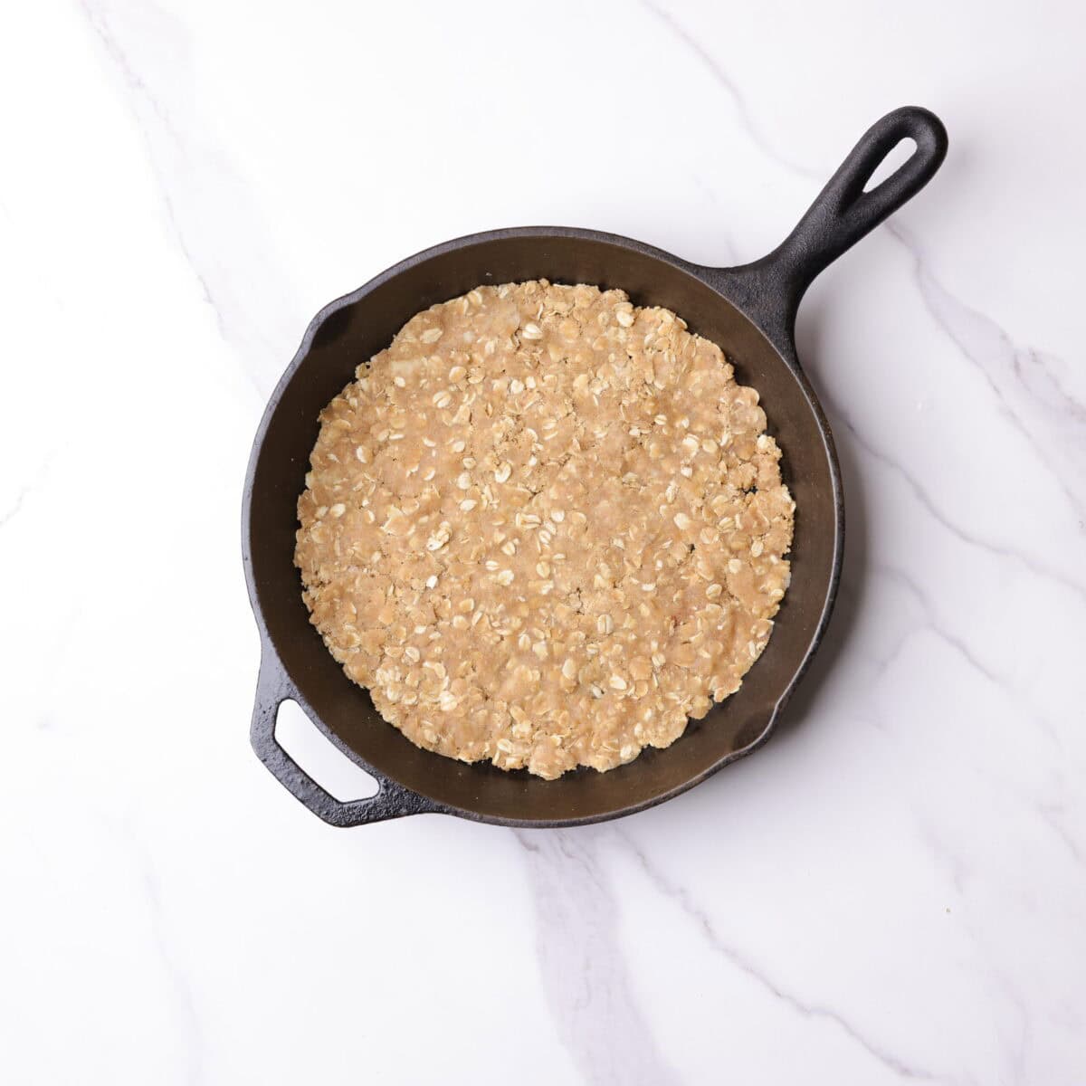 A skillet with the crumble mixture pressed into a thin layer that covers the bottom of the pan.