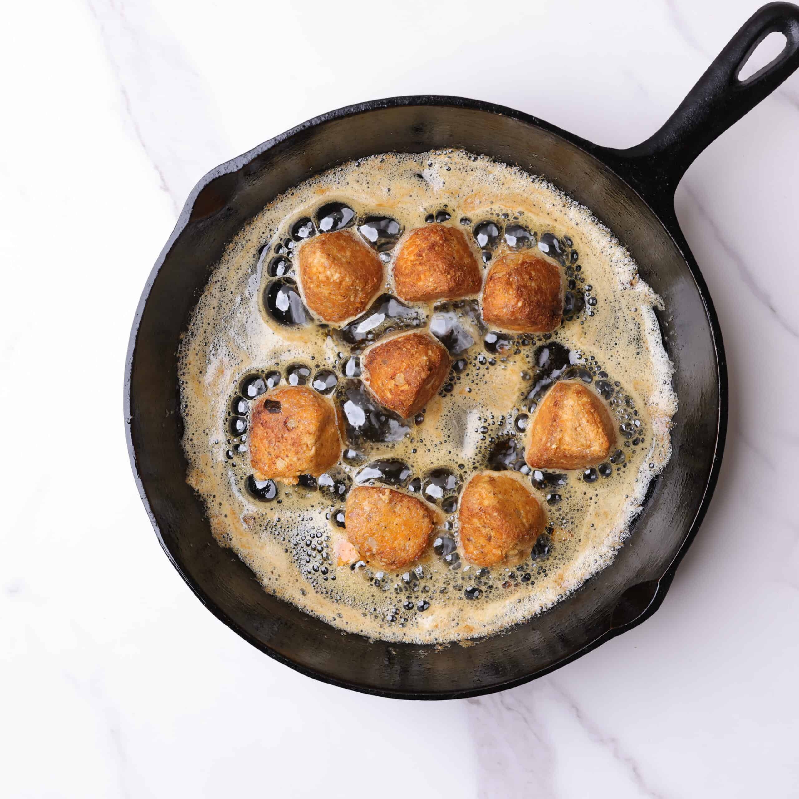 Skillet with hot oil and eight salmon meatballs fried to golden perfection.
