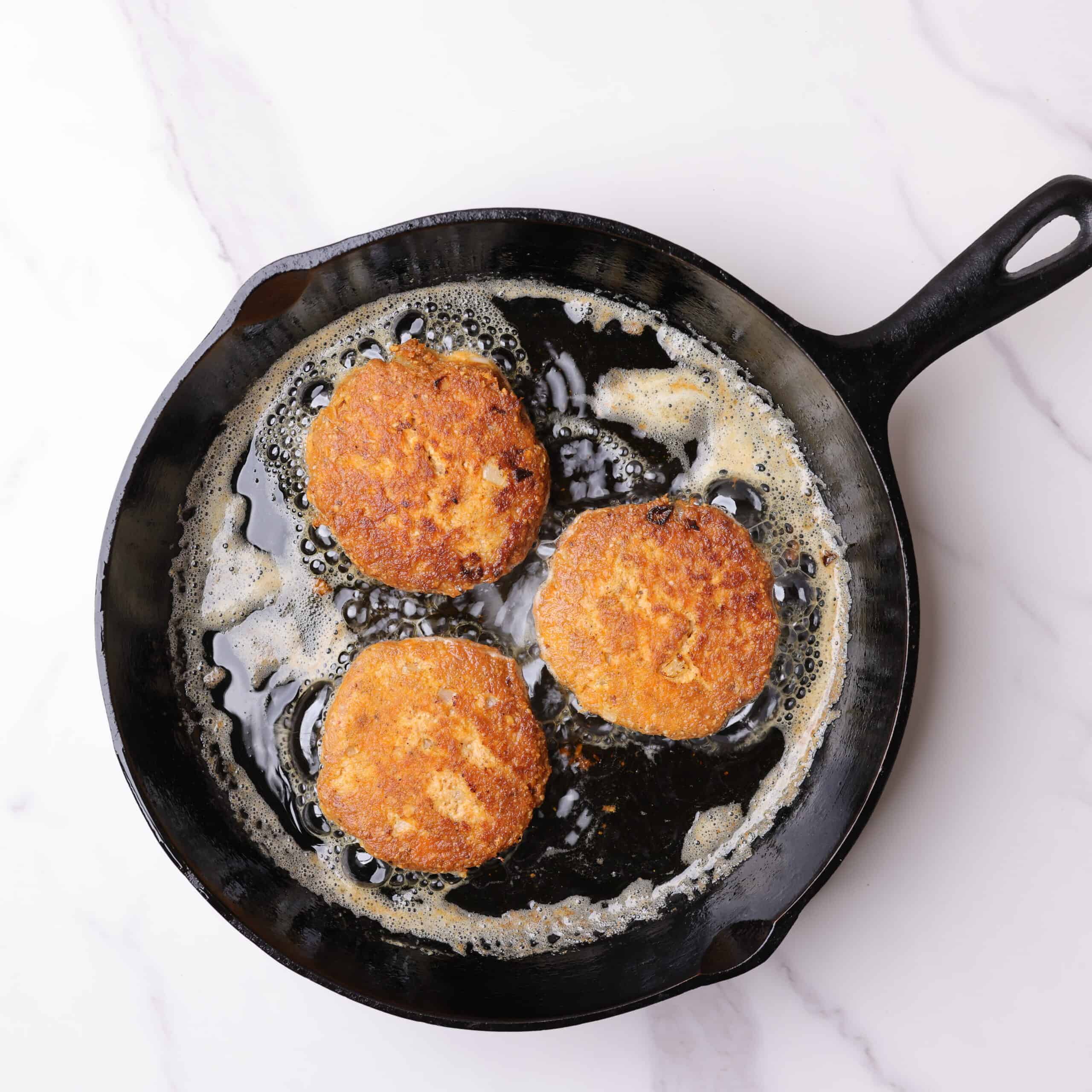 Skillet with hot oil and three smoked salmon patties fried to golden perfection.