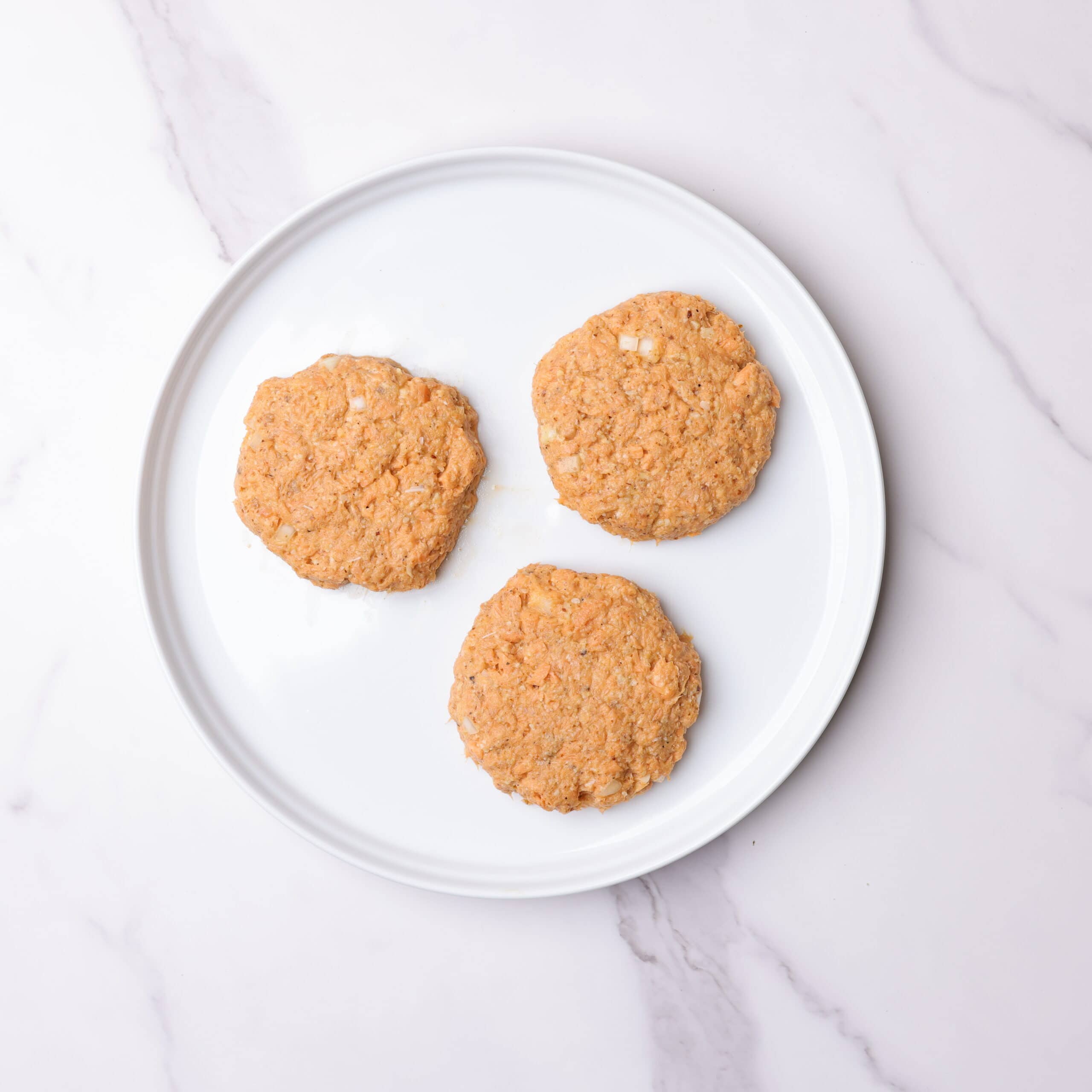A white plate with three formed salmon patties on it.
