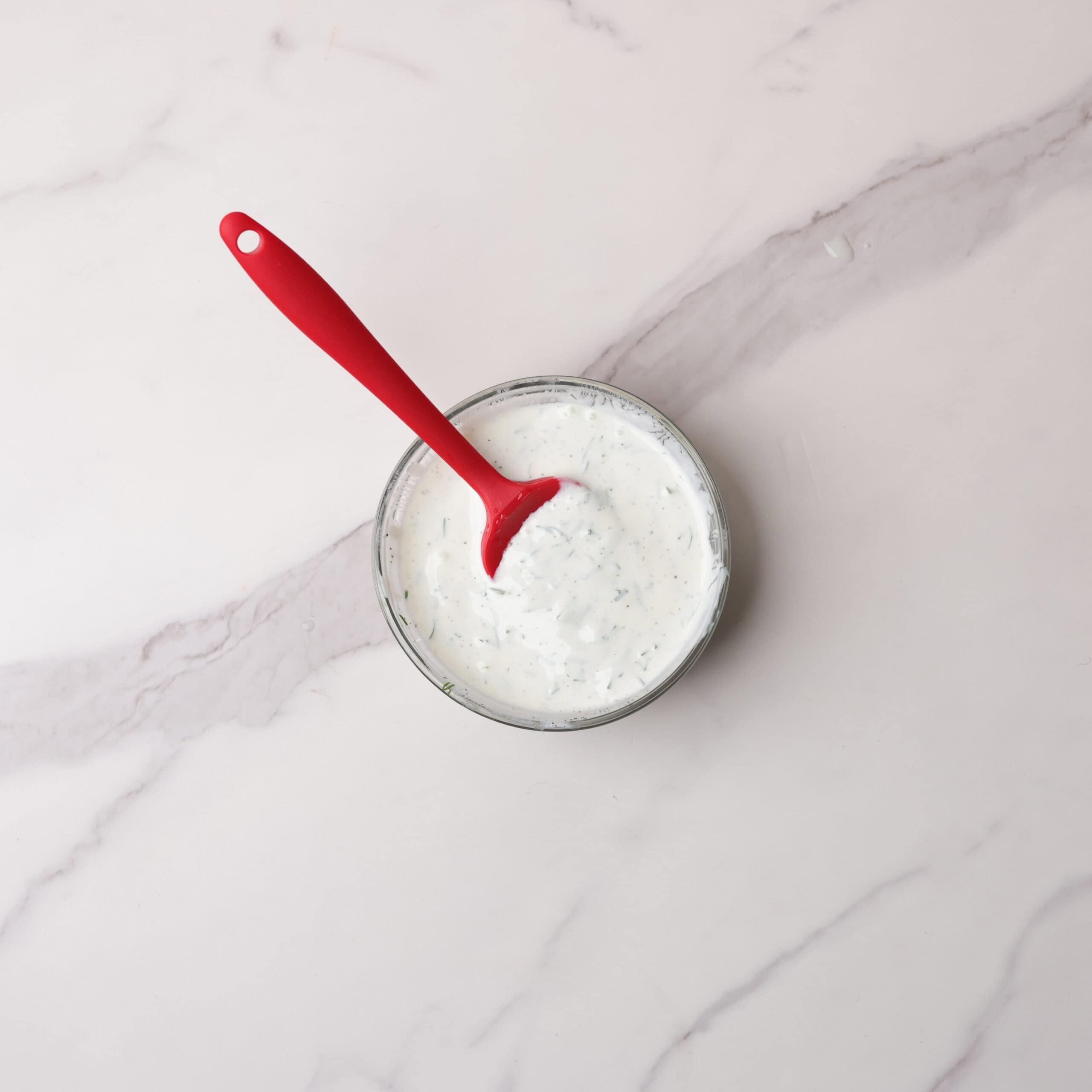 A glass bowl with the dill sauce mixed together with a red spatula in the bowl. 