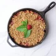 A cast iron skillet with a golden brown bake crisp garnished with mint leaves and a strawberry.