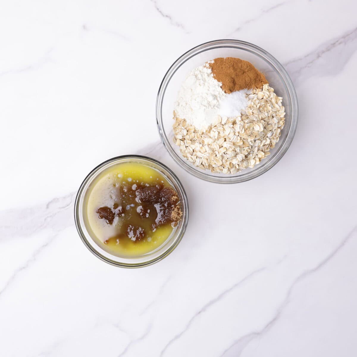 A small glass bowl with the melted butter poured over the brown sugar and another larger glass bowl containing the remaining dry ingredients for the crumble topping.