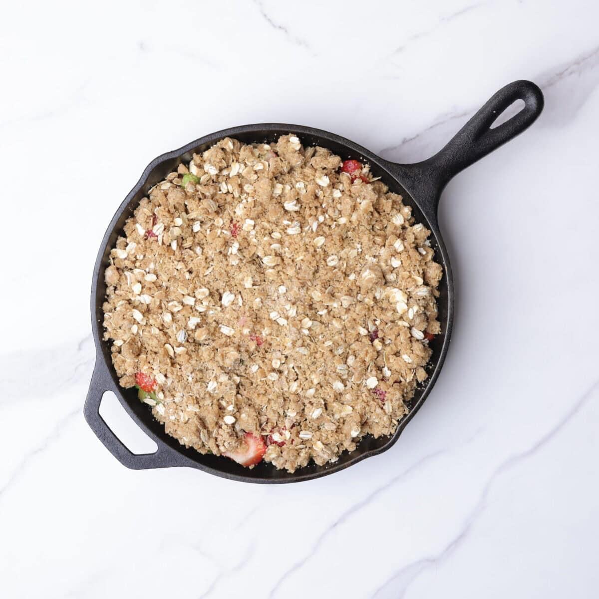 A cast iron skillet with the fruit mixture topped with the sugar and oat crumble. 