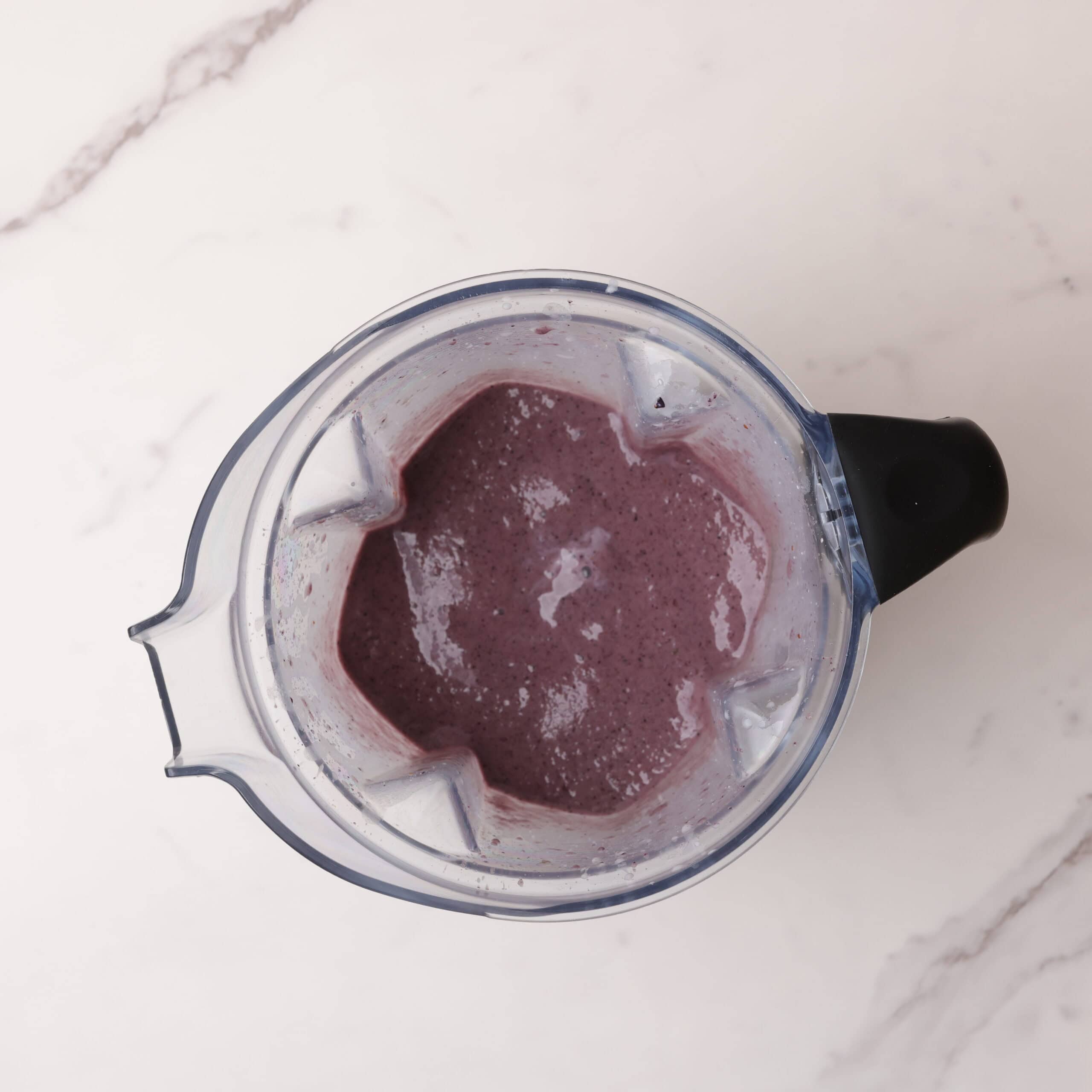 A vitamix with the blended blueberry smoothie in it.