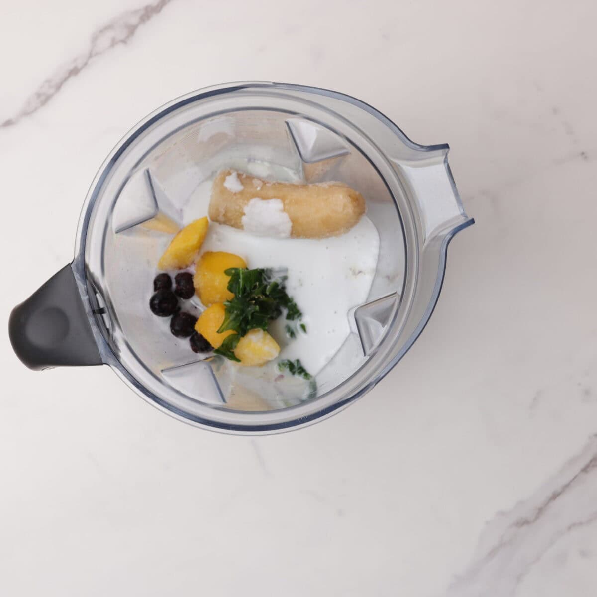 A vitamix with the milks and syrup poured over the frozen ingredients.