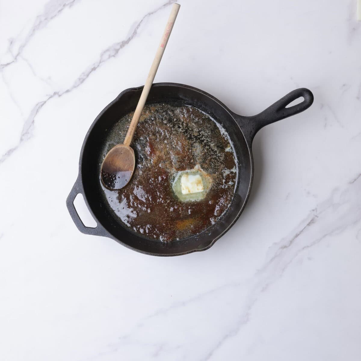 A skillet with melted butter, brown sugar and cinnamon in it with a wooden spoon for stirring.