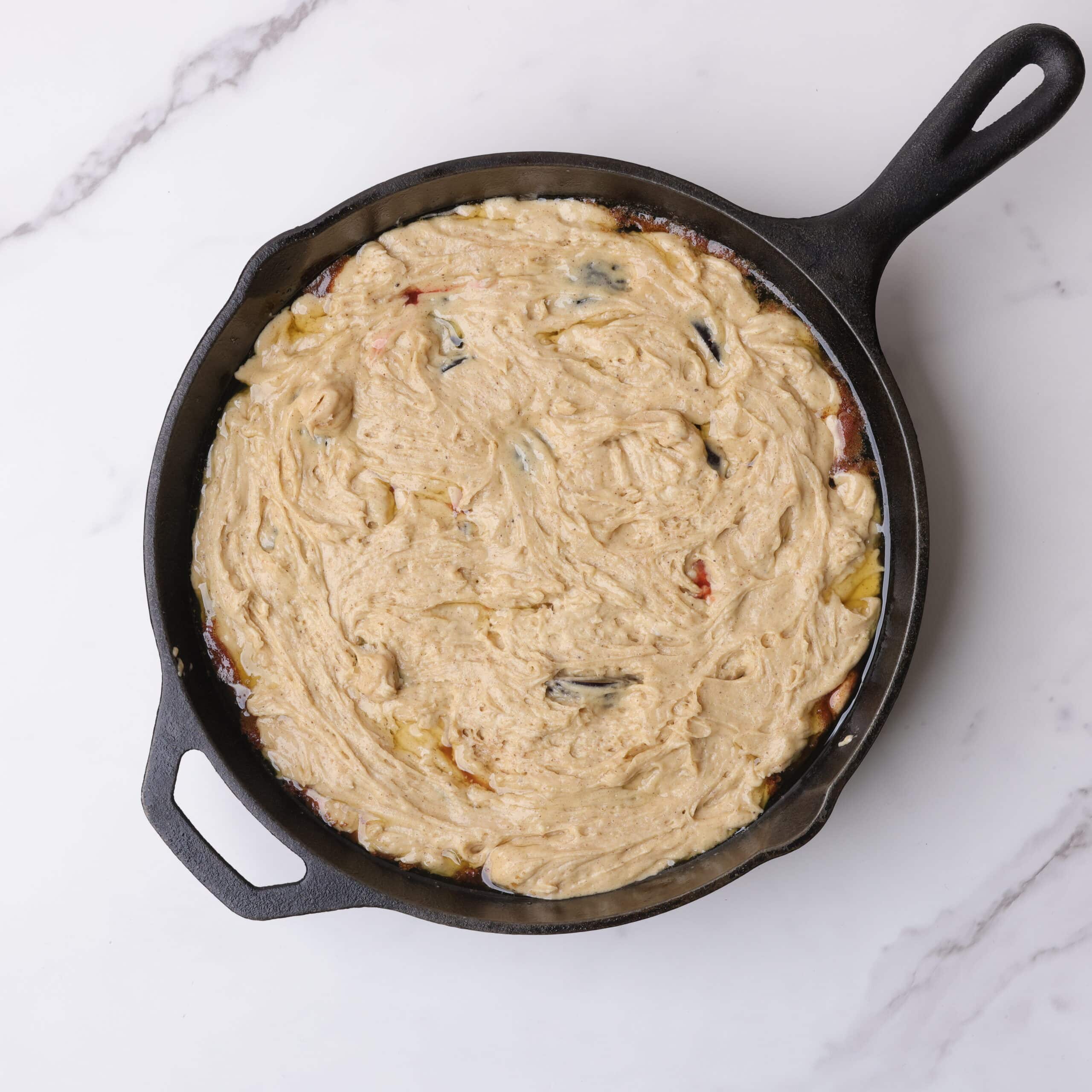 The skillet with the batter evenly spread over the cooked plums.