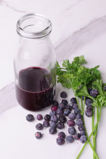 Blueberry Balsamic Vinaigrette in a bottle and displayed with parsley and a sprinkle of blueberries.