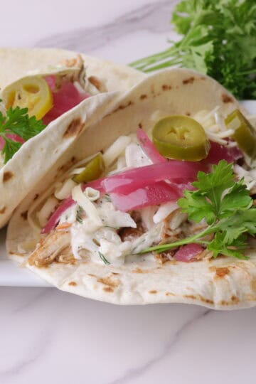 Barbecue Pulled Chicken Wrap garnished with pickled purple onions, pickled jalapenos and parsley displayed on a white plate.