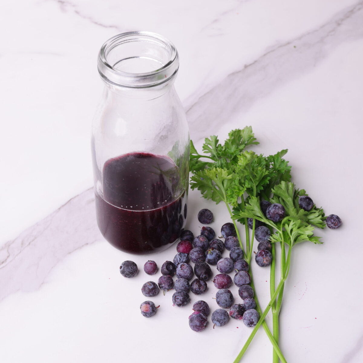 Blueberry Balsamic Vinaigrette in a bottle and displayed with parsley and a sprinkle of blueberries.