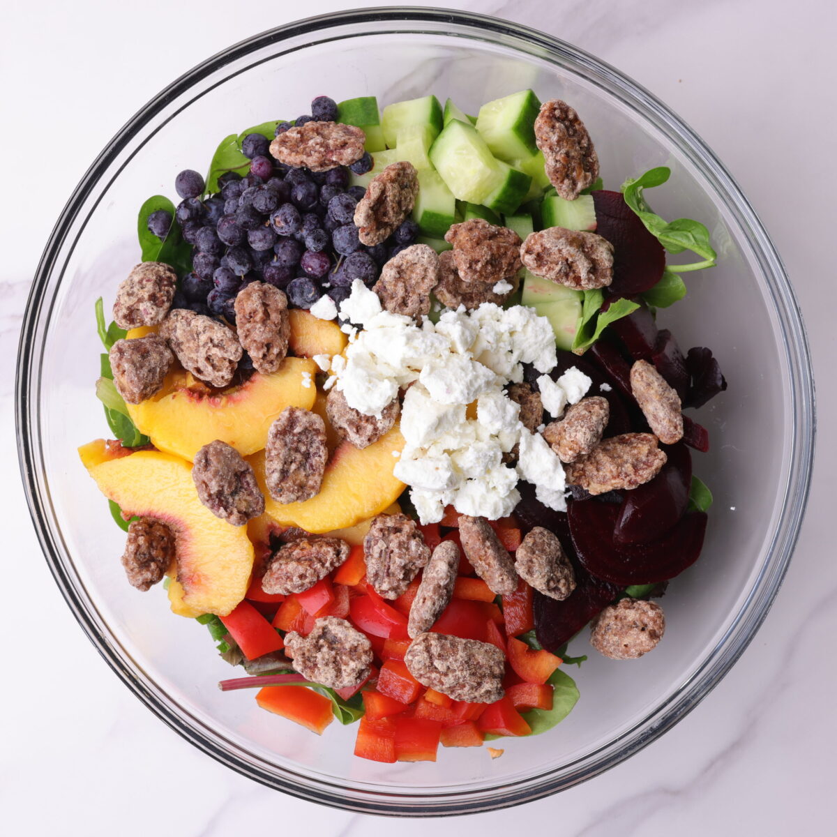 A glass bowl with all of the ingredients for the Peach and Blueberry Salad arranged.