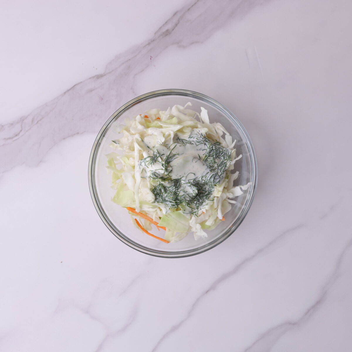 A small glass bowl with the cabbage mix topped with the coleslaw dressing, not yet mixed together.