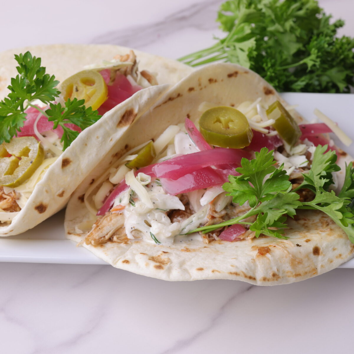 Barbecue Pulled Chicken Wrap garnished with pickled purple onions, pickled jalapenos and parsley displayed on a white plate. 