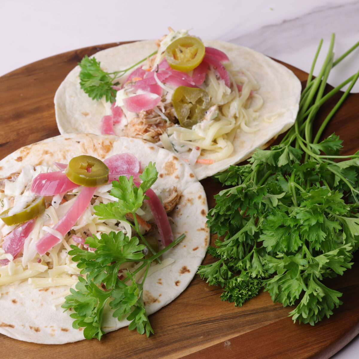 Two fully assembled pulled chicken wraps displayed on a wooden board and garnished with parsley.