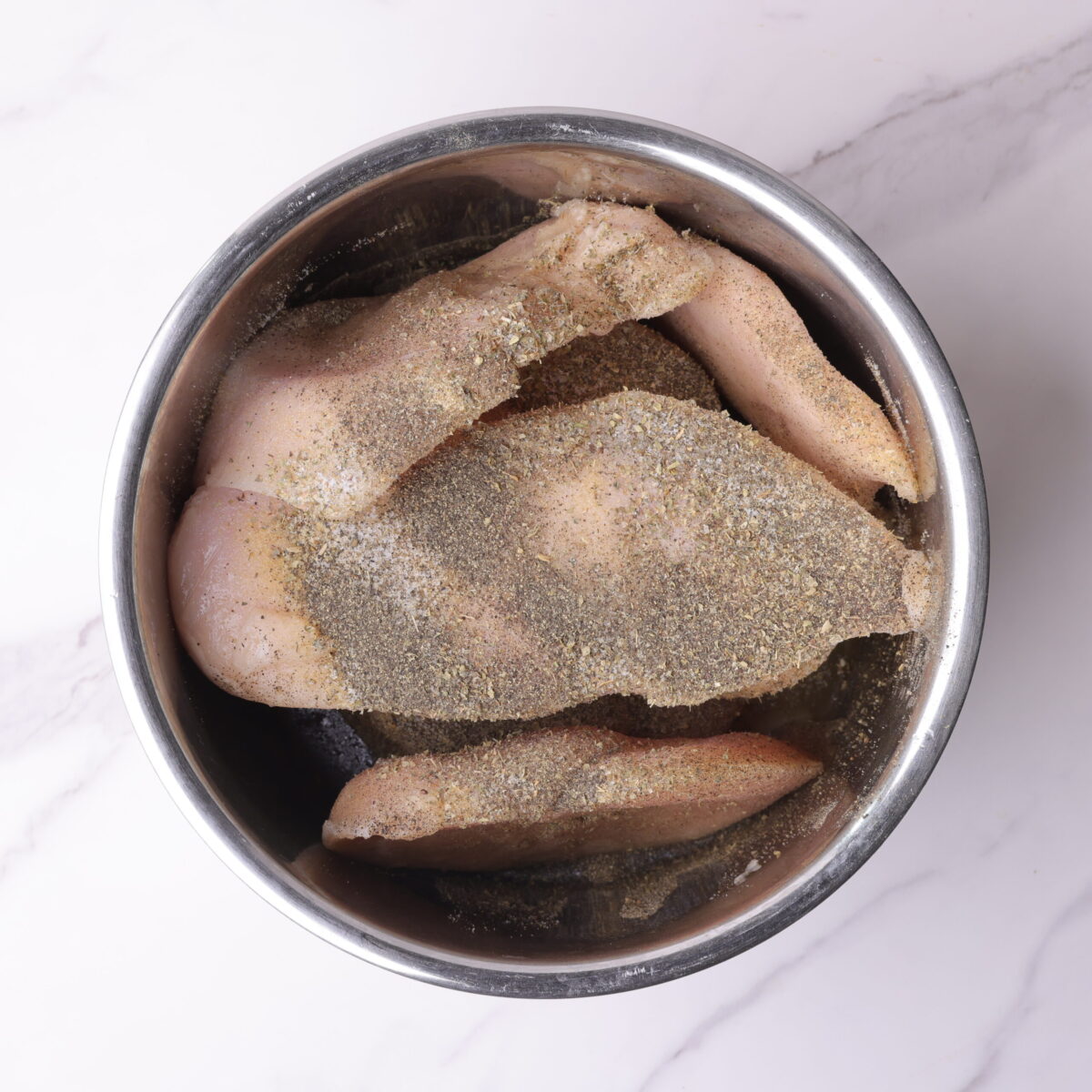 The instant pot bowl filled with the chicken breasts, chicken stock and sprinkled with all of the spices. 
