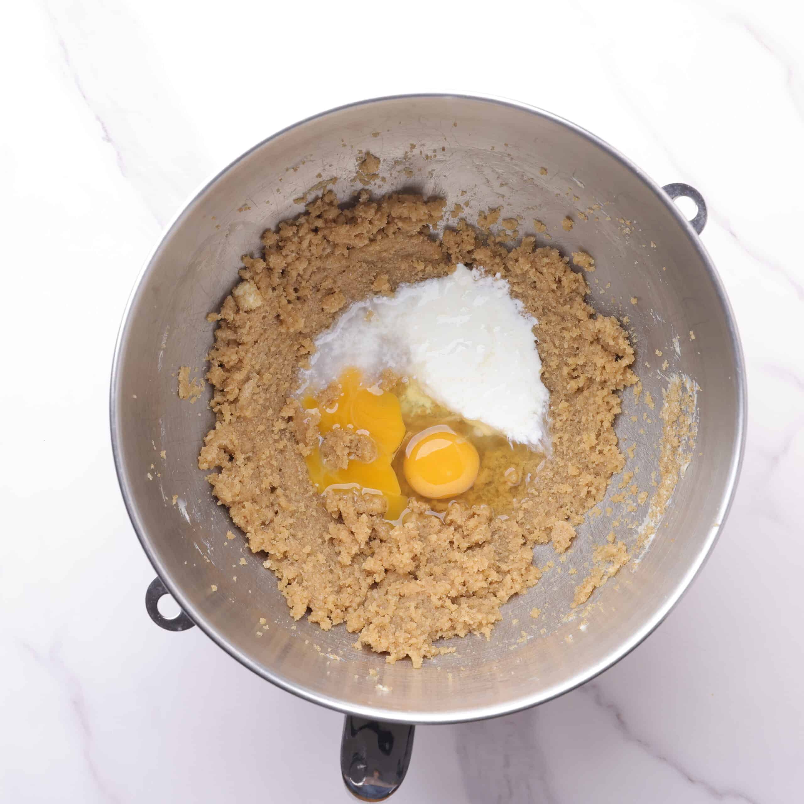 A mixing bowl with the butter and sugars mixed together and the liquids sitting on top, ready to be mixed in.