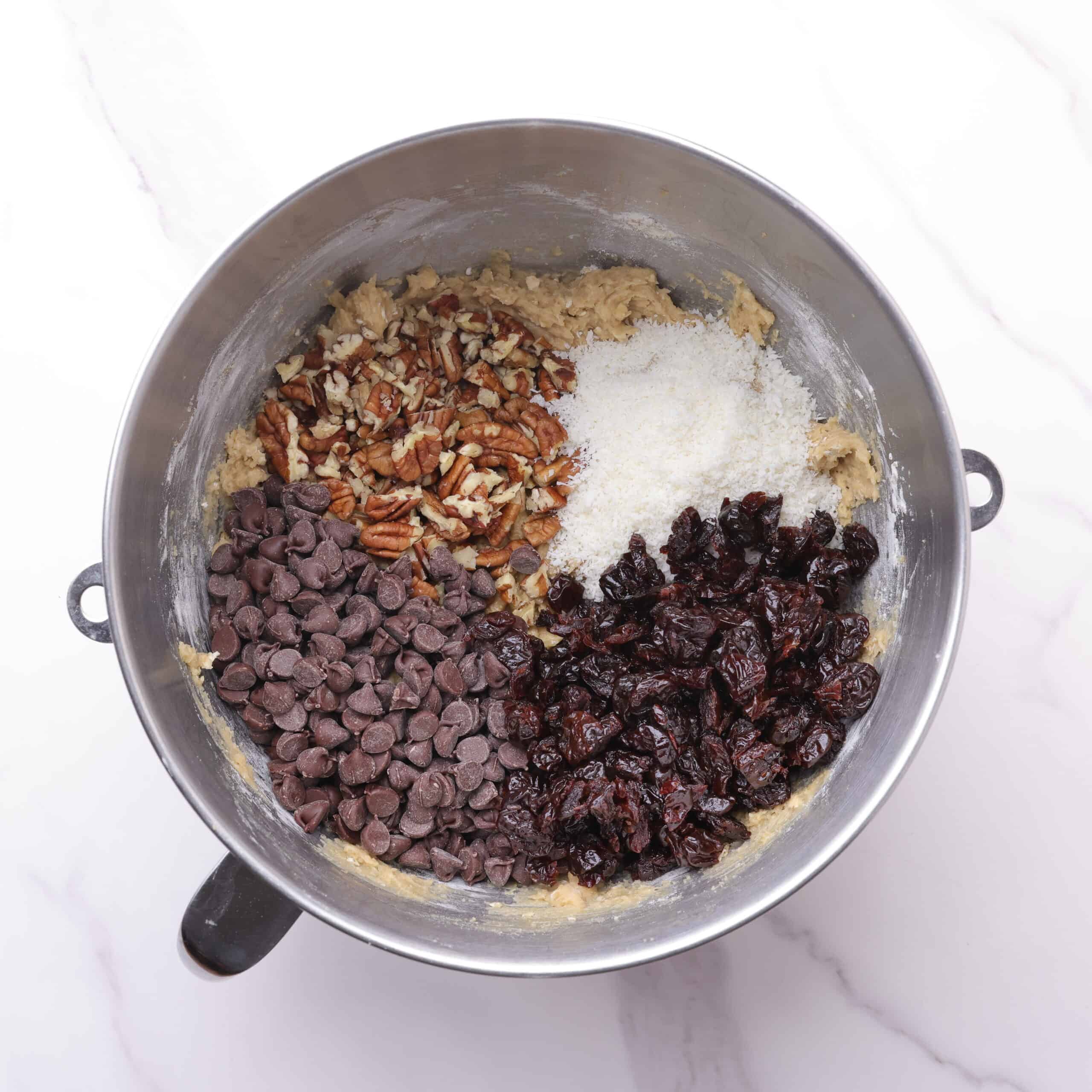 A mixing bowl with the batter for the oatmeal cherry cookies topped with all the mix ins.