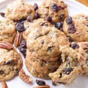 A white plate of Oatmeal Cherry Cookies with three stacked in the middle and one bitten out of leaning against them.