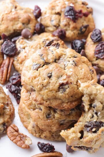 A white plate of Oatmeal Cherry Cookies with three stacked in the middle and one bitten out of leaning against them.