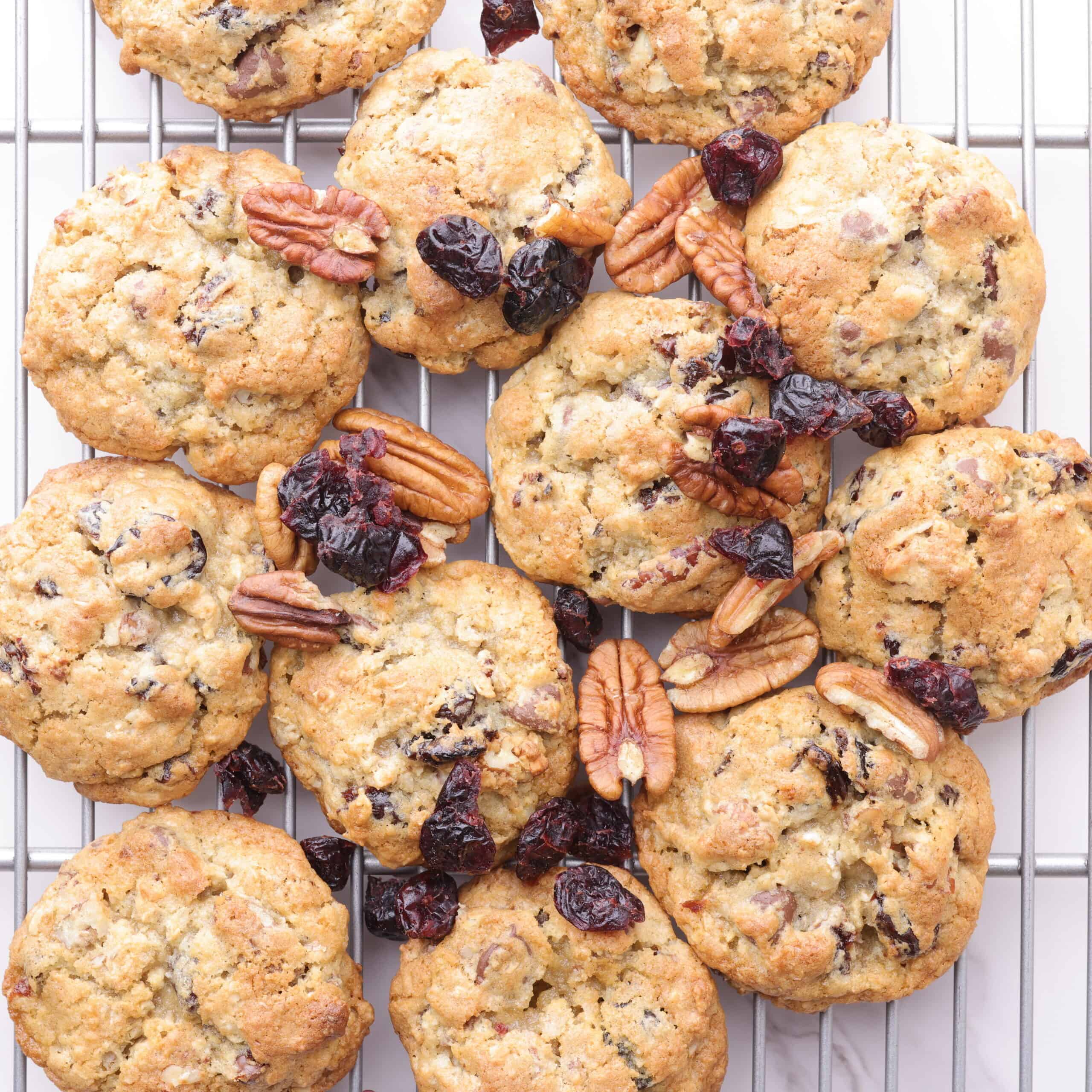 A wire rack with golden brown cookies sprinkled with pecans and dried cherries on it.